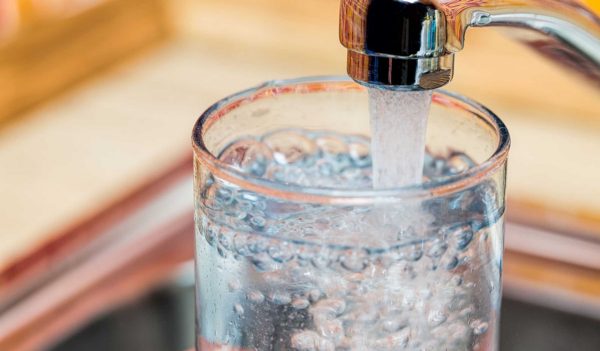 Closeup shot of a man pouring a glass of fresh water from a kitchen faucet