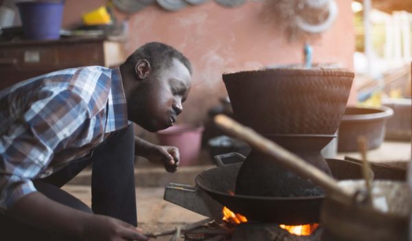 African man sitting to blow fire to cook rice