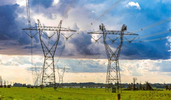 High voltage transmission towers in a field against a cloudy sky.