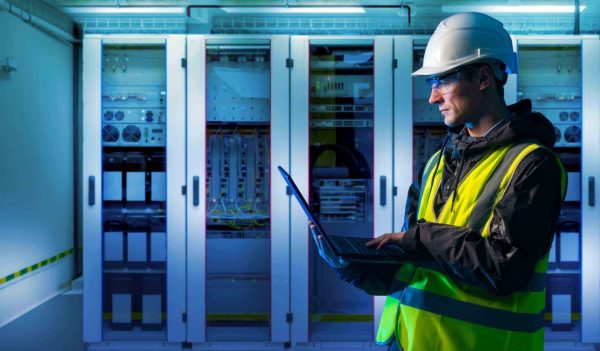Male engineering working on a laptop in PPE in a server room.