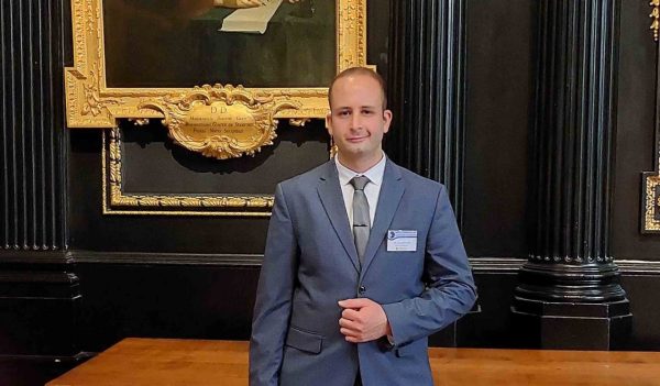 Ahmad Helmi standing in front of a black wall with columns and a gold framed image in the background.