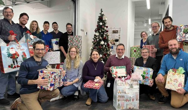 Group image of Stantec team holding presents around a Christmas tree for donation to Operation Santa Claus.