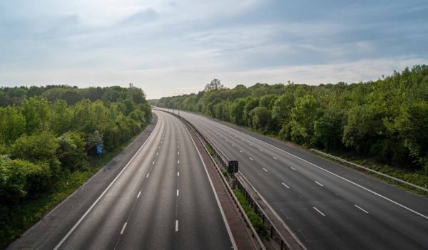Empty M20 motorway during the day, showing roads surrounded by trees, on a cloudy day.