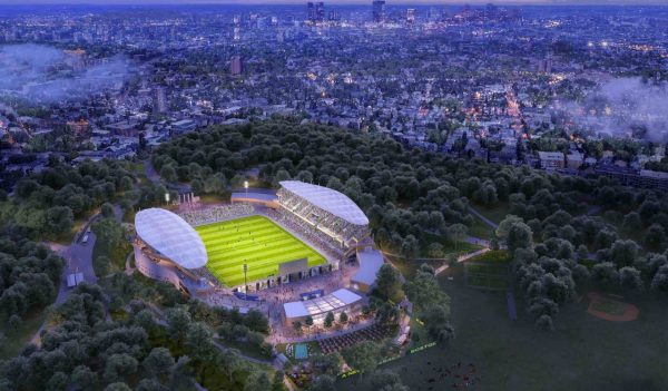 Aerial rendering of a new soccer stadium surrounded by trees, playing fields, and the city beyond all lit up at night