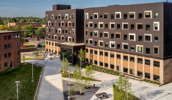 Exterior of student housing buildings with a central courtyard in the middle with sidwalks, landscaping and benches for seating.