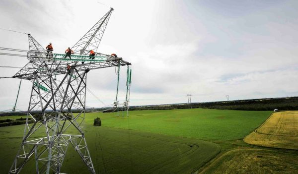 Workers on the top of a high voltage power line tower.