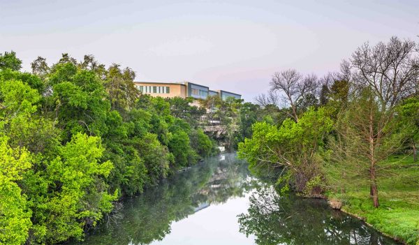 A small river with trees and the exterior school in the distance