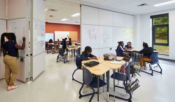 Students two classrooms separated by a partition wall that is a whiteboard - workign at desks that can fit together.