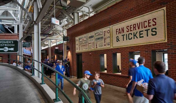 Interior concourse area with fans walking along a brick wall tht is the fan services / ticketing area.