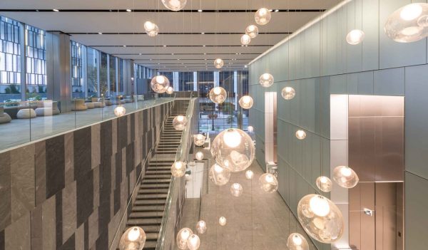 Interior main lobby from the second floor, looking down with stairs in the distance and globe lights hanging from ceiling.
