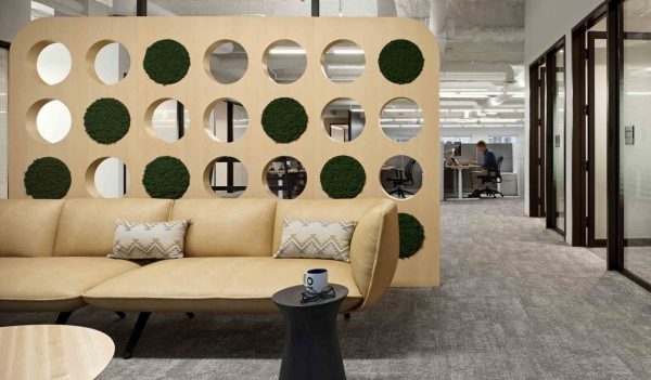 Interior employee common area with tan sofa in front of a feature wall with circle cut-outs and greenery in some of the cut outs.