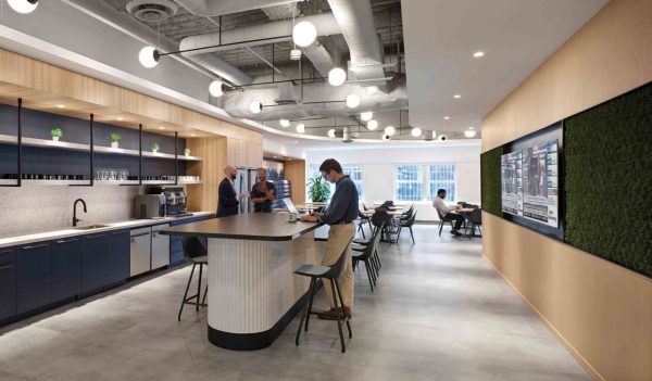 Interior staff cafe area with kitchen, island with seating and a natural wood feature wall with a band of green in the middle to simulate grass.