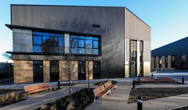 Image of building exterior, showing blue sky behind and benches with green grass in front 