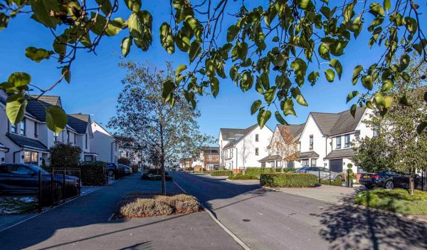 Residential street with rows of white town homes on either side with a blue sky and trees.