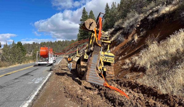 Construction equipment digging trenches alongside a remote roadway to install fibre optic cable.