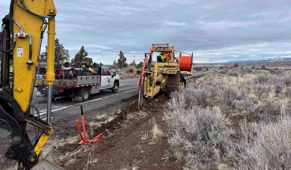 Construction equipment digging trenches alongside a remote roadway to install fibre optic cable. 